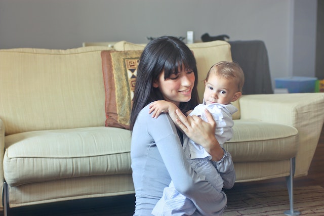 A nanny in Gray sweater carrying a toddler